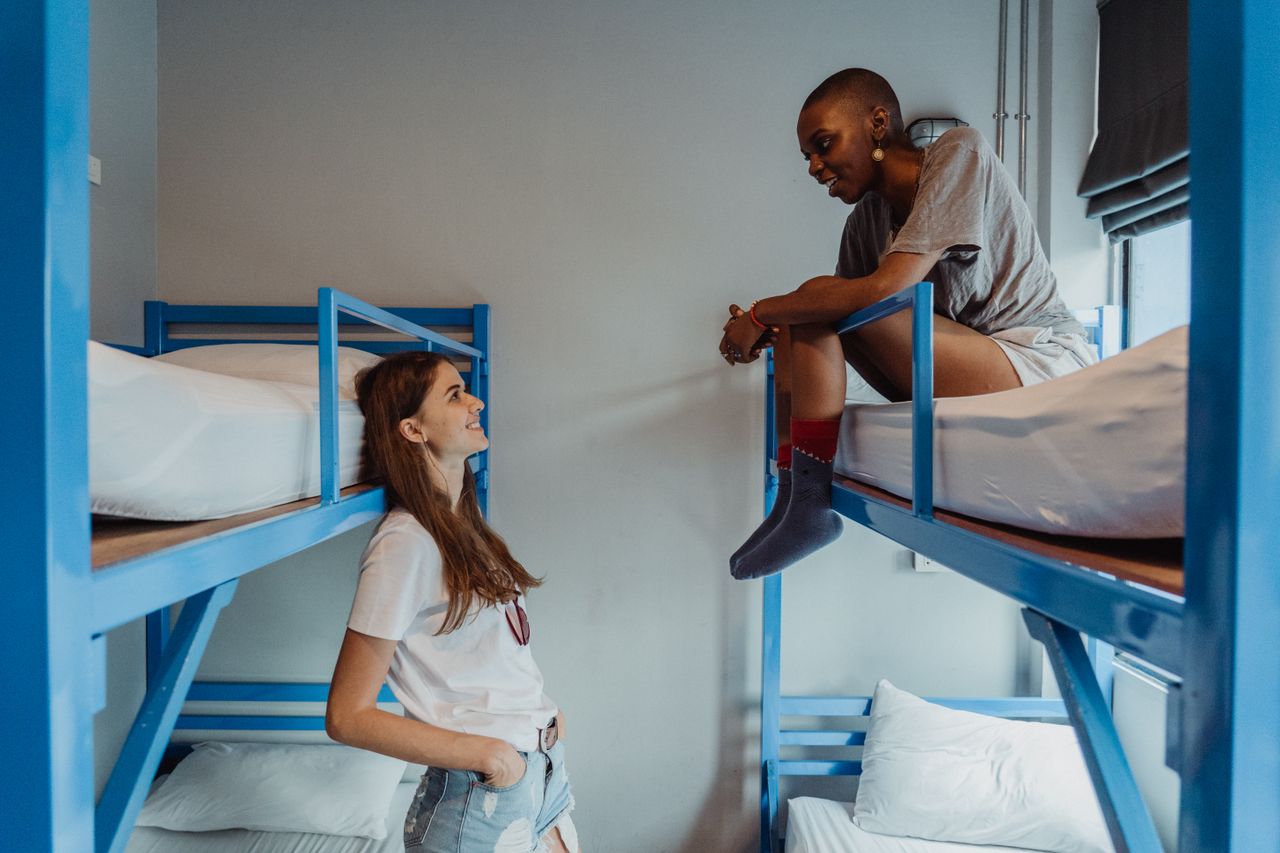 Two women talking and relaxing in a modern hostel room with bunk beds.